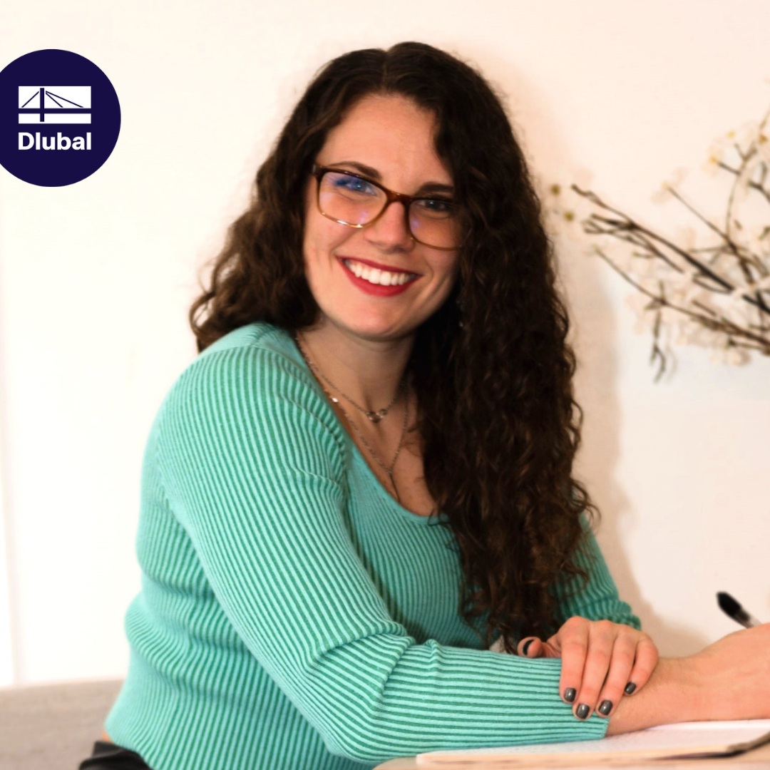 Katie, nová kolegyně, se usmívá do kamery v kancelářském oblečení.