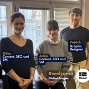 Tři noví členové týmu v kanceláři Dlubal v Praze, Eliška a Adéla z týmu Content-SEO-Social-Media a Vojtěch jako grafik, stojí před okny s výhledem na staré pražské budovy