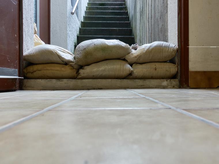 Schutzmaßnahmen gegen Überschwemmungen in Kellern. Die Barriere aus Sandsäcken liegt im Eingangsbereich eines Wohngebäudes. Betonstufen führen nach oben.