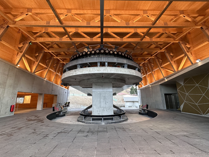 Innenansicht der Talstation mit 3S-Seilbahnen, Stahlkonstruktion, Holzdach und Betonboden.