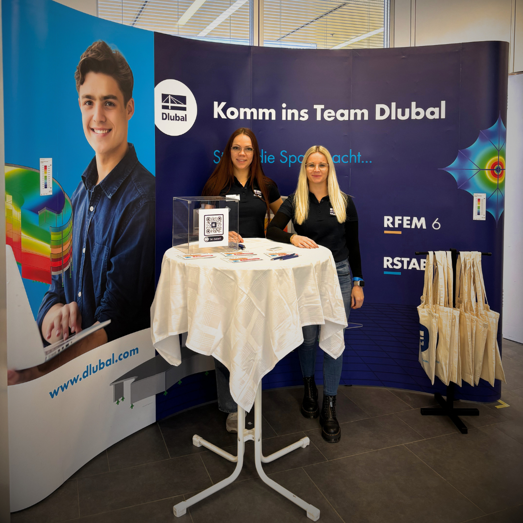 Dlubal-Mitarbeiterinnen am blau gebrandeten Messestand auf der WIK-Leipzig 2025 mit RFEM- und RSTAB-Elementen, Stehtisch mit Flyern und QR-Code sowie Dlubal-Stofftaschen