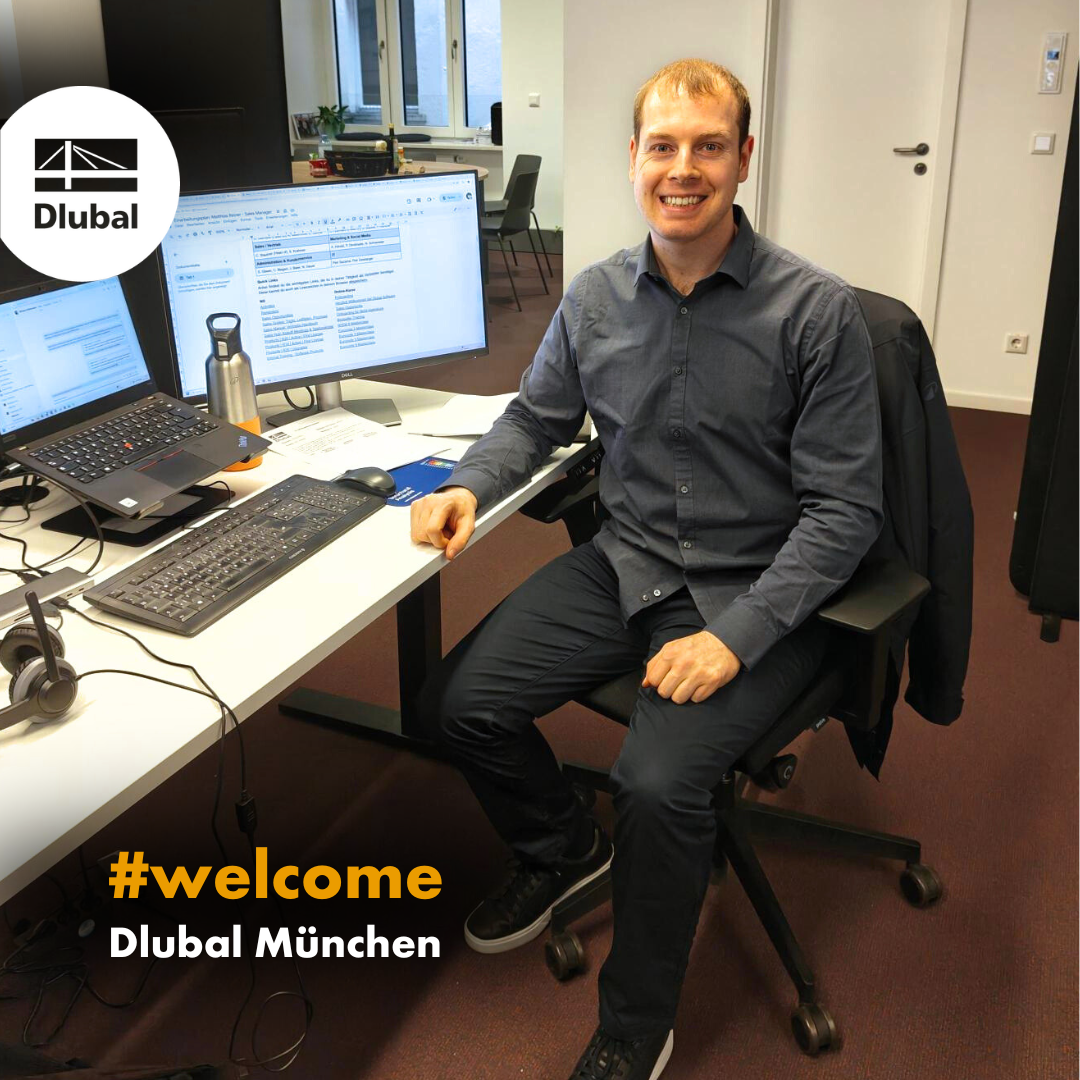 Neuer Mitarbeiter sitzt lächelnd an Schreibtisch im Dlubal Büro München