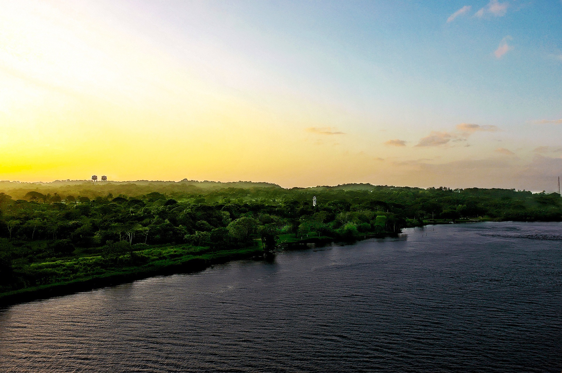 Weitläufige Landschaft mit Vegetation und Wasserfläche entlang des Panama-Kanals, umgeben von grünen Hügeln und Bäumen.