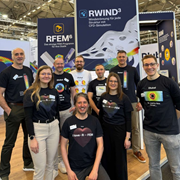 Eine Gruppe von Ingenieuren, die ein Tragwerksmodellprojekt besprechen, in professioneller Kleidung und in einer technischen Büroumgebung stehend.