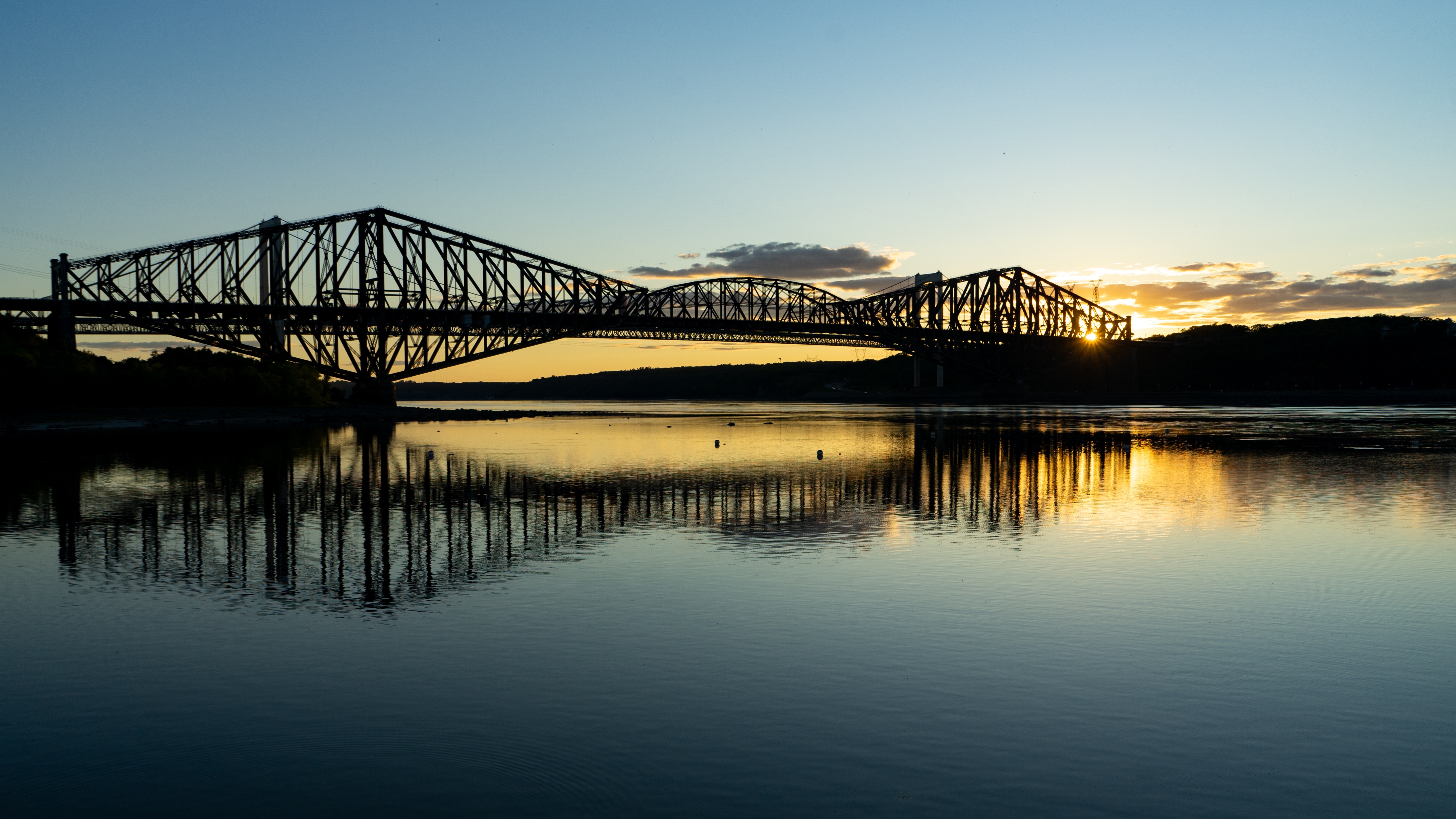 Die Québec-Brücke ragt majestätisch in der Morgendämmerung in den Himmel und spiegelt sich im stillen Wasser wider.