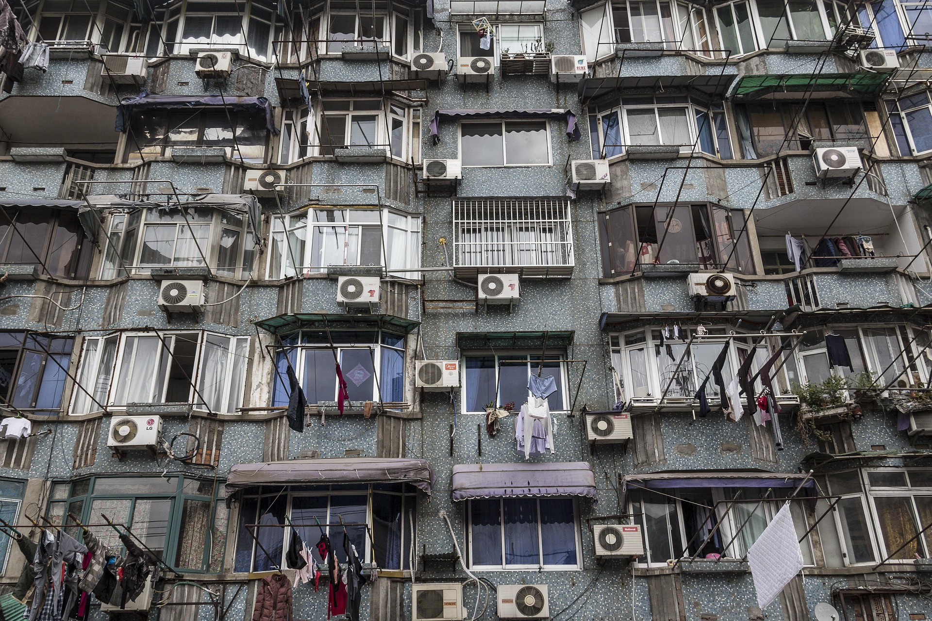 Fassade eines Wohnhauses mit zahlreichen Klimaanlagen, die zur städtischen Überhitzung beitragen, da die Abwärme durch engstehende Gebäude nicht entweichen kann.