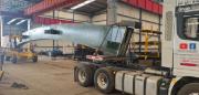 In einer Metallwerkstatt wird ein Stahlbogenträger für eine Brücke mit Kränen angehoben und auf einen Lastwagen verladen.