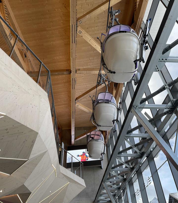 Interior view of the station with cable cars and skiers in the background.