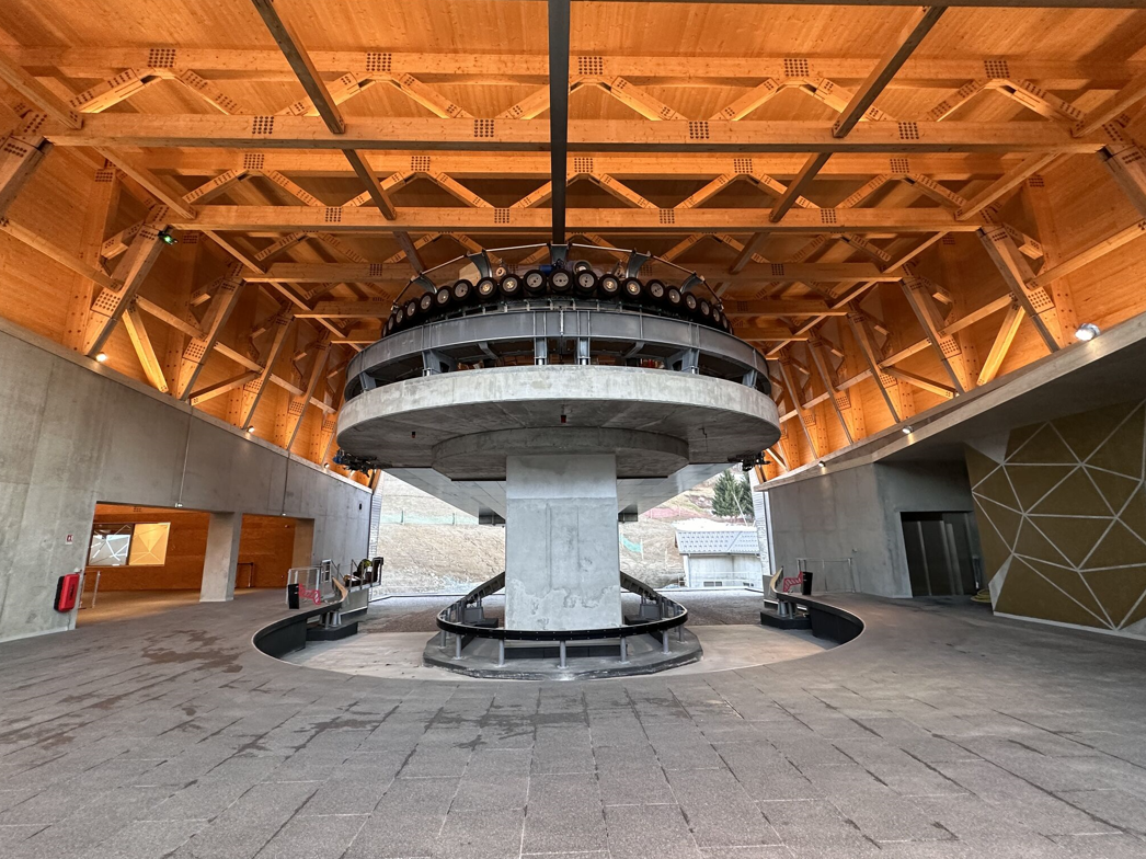 Interior view of the valley station with 3S cable cars, steel structure, timber roof, and concrete floor.