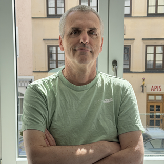 Dlubal team member standing in front of office windows with arms crossed and a friendly expression.