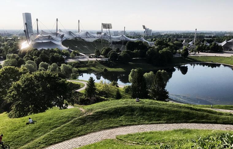 The artificially created environment around the Olympic Stadium in Munich is shown. Architectural elements and green spaces are visible.