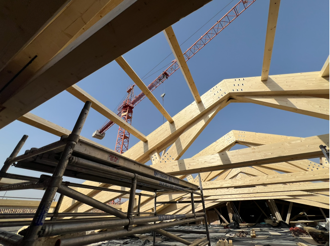 Cerchas de madera grandes siendo instaladas en un sitio de construcción con una grúa de alta capacidad para soportar la carga.