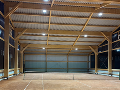 Vista interior de un amplio pabellón de tenis con estructura de madera.