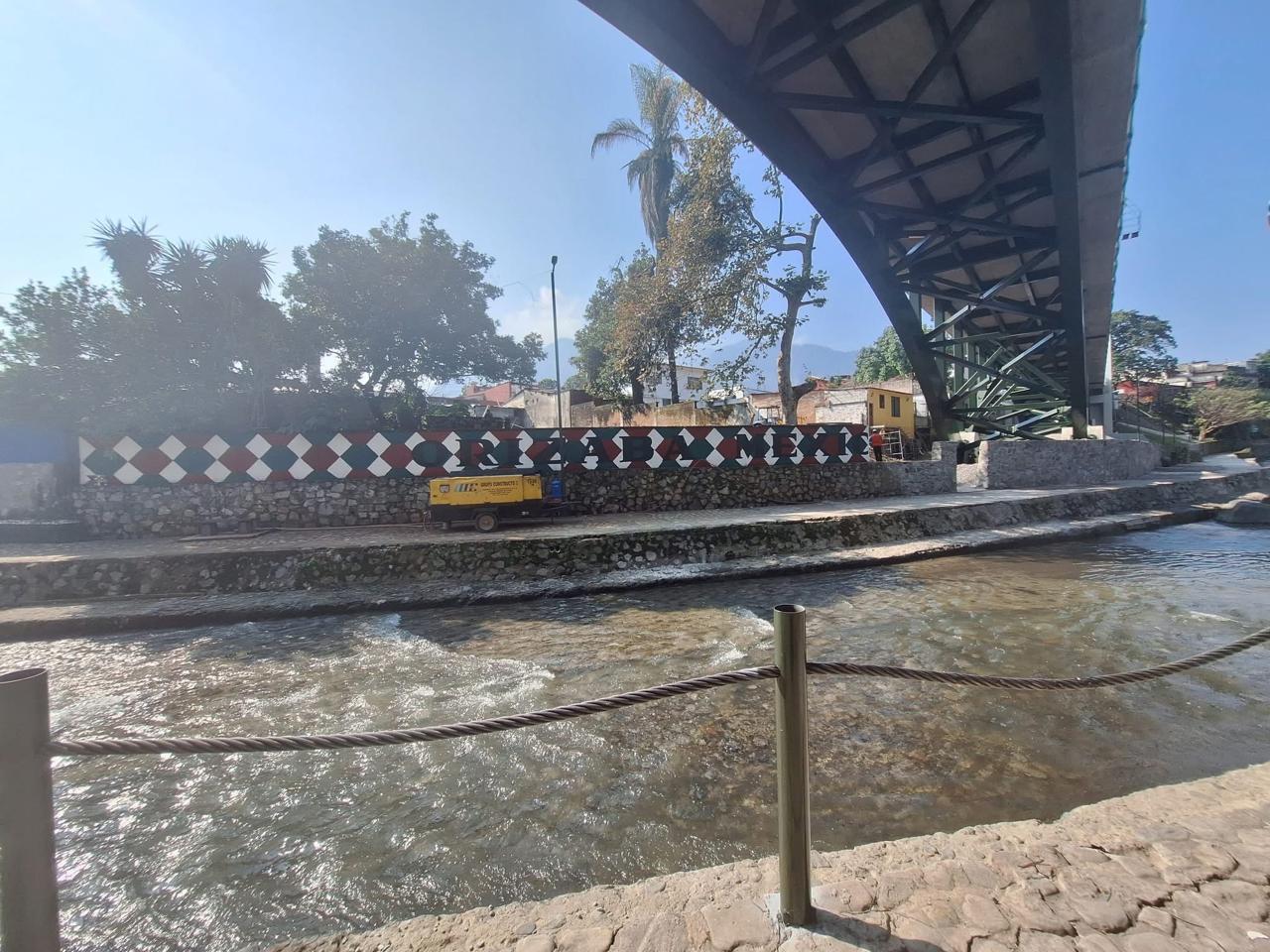 Vista inferior de un puente de arco de acero que cruza el río Orizaba en Veracruz, con muro decorado y cauce fluvial