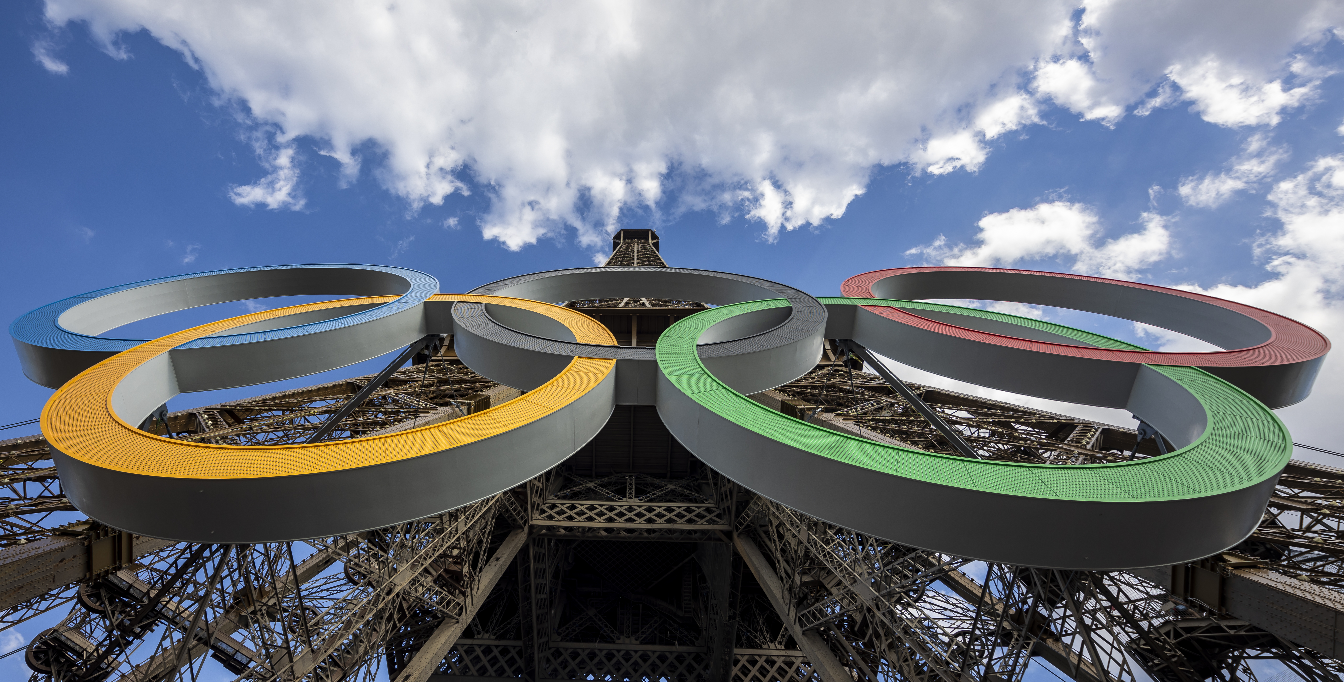 Contre-plongée des cinq anneaux olympiques sur la tour Eiffel sous un ciel bleu