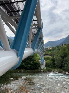 Estrutura de aço de uma ponte para peões curva sobre um rio com paisagem alpina ao fundo